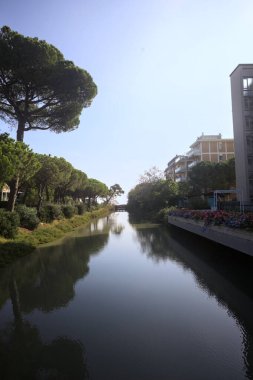 Deniz kıyısındaki bir italyan kasabasında bir korulukla suya atılan binaların arasından geçen bir nehir.