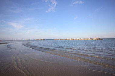Gün batımında dalgaların çekildiği kumsalda, uzakta bir kaya dalgası var.