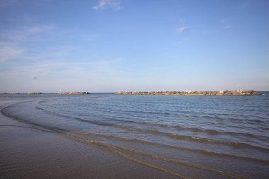 Gün batımında dalgaların çekildiği kumsalda, uzakta bir kaya dalgası var.