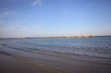 Gün batımında dalgaların çekildiği kumsalda, uzakta bir kaya dalgası var.