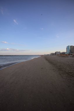 Gün batımında dalgaların çekildiği kumsalda, uzakta bir kaya dalgası var.