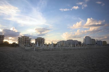 Gün batımında plajın yanındaki binalar boş bir sahil beldesinin arkasından görülüyor.