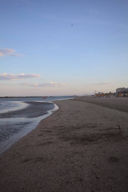 Gün batımında dalgaların çekildiği kumsalda, uzakta bir kaya dalgası var.