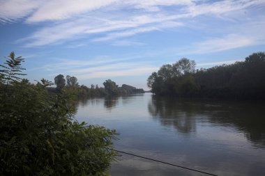 İtalya 'nın kırsal kesimlerinde kısmen bulutlu bir günde sudaki ağaçlarla çevrili bir nehir.