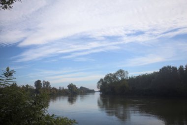 İtalya 'nın kırsal kesimlerinde kısmen bulutlu bir günde sudaki ağaçlarla çevrili bir nehir.