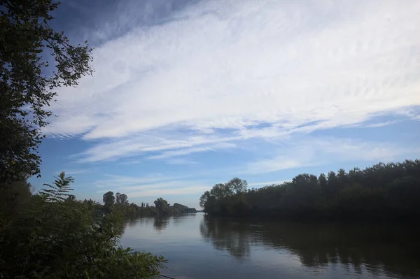 İtalya 'nın kırsal kesimlerinde kısmen bulutlu bir günde sudaki ağaçlarla çevrili bir nehir.