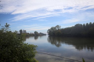 İtalya 'nın kırsal kesimlerinde kısmen bulutlu bir günde sudaki ağaçlarla çevrili bir nehir.
