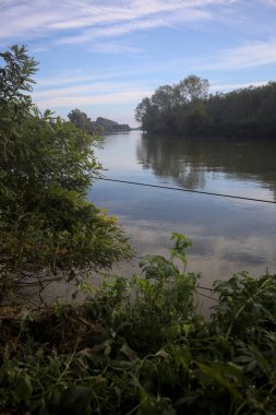 İtalya 'nın kırsal kesimlerinde kısmen bulutlu bir günde sudaki ağaçlarla çevrili bir nehir.