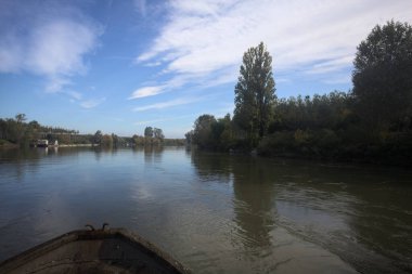 Nehir, sudaki ağaçlarla ve sahneyi çerçeveleyen dubalarla çevrili.