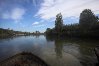Nehir, sudaki ağaçlarla ve sahneyi çerçeveleyen dubalarla çevrili.