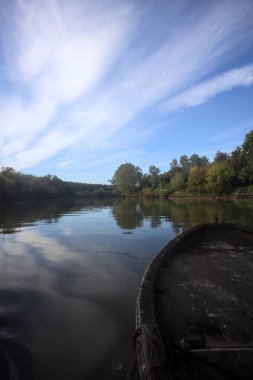 Nehir, sudaki ağaçlarla ve sahneyi çerçeveleyen dubalarla çevrili.