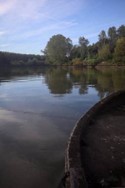 Nehir, sudaki ağaçlarla ve sahneyi çerçeveleyen dubalarla çevrili.