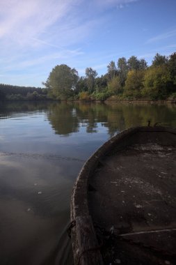 Nehir, sudaki ağaçlarla ve sahneyi çerçeveleyen dubalarla çevrili.