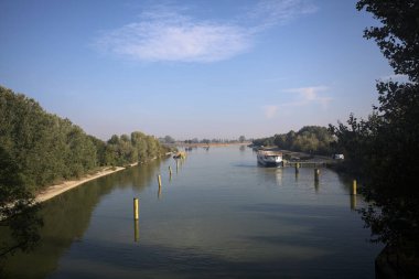 Oyalama kanalı, direkleri olan ve suya gökyüzü düşmüş demirli bir tekne ve sahneyi çerçeveleyen bir ağaç.