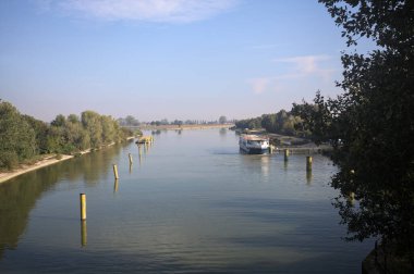 Oyalama kanalı, direkleri olan ve suya gökyüzü düşmüş demirli bir tekne ve sahneyi çerçeveleyen bir ağaç.