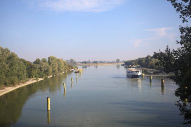 Oyalama kanalı, direkleri olan ve suya gökyüzü düşmüş demirli bir tekne ve sahneyi çerçeveleyen bir ağaç.