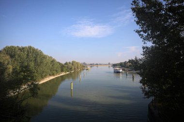 Oyalama kanalı, direkleri olan ve suya gökyüzü düşmüş demirli bir tekne ve sahneyi çerçeveleyen bir ağaç.