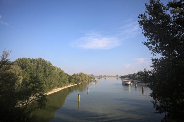Oyalama kanalı, direkleri olan ve suya gökyüzü düşmüş demirli bir tekne ve sahneyi çerçeveleyen bir ağaç.