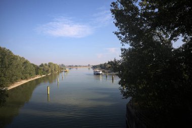 Oyalama kanalı, direkleri olan ve suya gökyüzü düşmüş demirli bir tekne ve sahneyi çerçeveleyen bir ağaç.