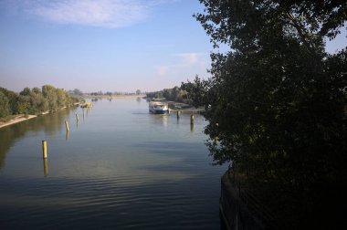 Oyalama kanalı, direkleri olan ve suya gökyüzü düşmüş demirli bir tekne ve sahneyi çerçeveleyen bir ağaç.