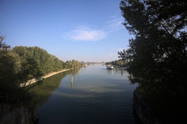 Oyalama kanalı, direkleri olan ve suya gökyüzü düşmüş demirli bir tekne ve sahneyi çerçeveleyen bir ağaç.