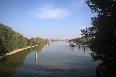 Oyalama kanalı, direkleri olan ve suya gökyüzü düşmüş demirli bir tekne ve sahneyi çerçeveleyen bir ağaç.