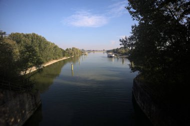 Oyalama kanalı, direkleri olan ve suya gökyüzü düşmüş demirli bir tekne ve sahneyi çerçeveleyen bir ağaç.