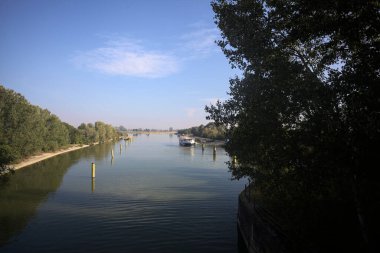 Oyalama kanalı, direkleri olan ve suya gökyüzü düşmüş demirli bir tekne ve sahneyi çerçeveleyen bir ağaç.