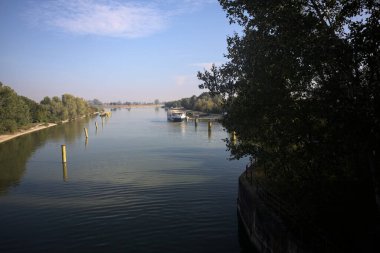 Oyalama kanalı, direkleri olan ve suya gökyüzü düşmüş demirli bir tekne ve sahneyi çerçeveleyen bir ağaç.