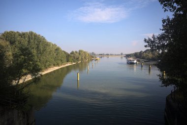 Oyalama kanalı, direkleri olan ve suya gökyüzü düşmüş demirli bir tekne ve sahneyi çerçeveleyen bir ağaç.