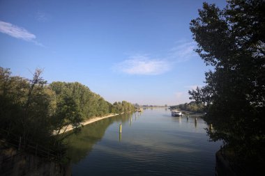 Oyalama kanalı, direkleri olan ve suya gökyüzü düşmüş demirli bir tekne ve sahneyi çerçeveleyen bir ağaç.