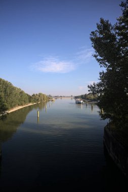 Oyalama kanalı, direkleri olan ve suya gökyüzü düşmüş demirli bir tekne ve sahneyi çerçeveleyen bir ağaç.