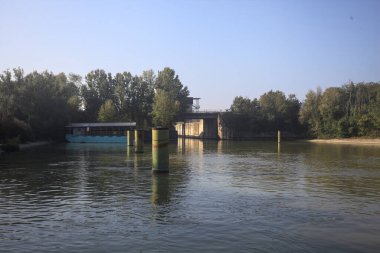 Kıyıların yanında demirleme direkleri ve güneşli bir günde İtalyan kırsalında ağaçlarla çevrili bir yol köprüsü olan saptırıcı bir kanal.