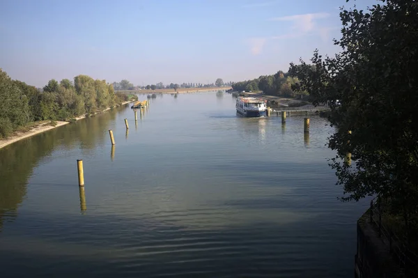 Oyalama kanalı, direkleri olan ve suya gökyüzü düşmüş demirli bir tekne ve sahneyi çerçeveleyen bir ağaç.