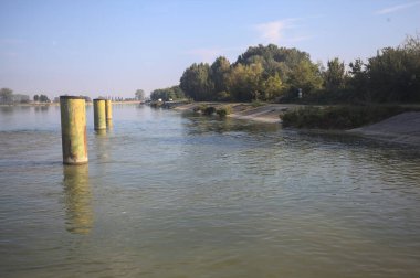 İtalya kırsalında güneşli bir günde beton kıyıdan görülen suya demirleme direkleri yansıyan saptırma kanalı.