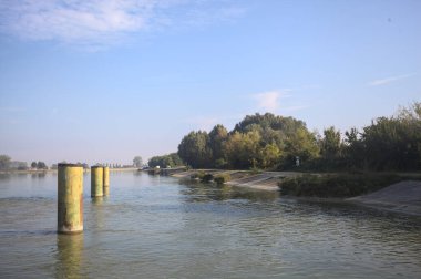 İtalya kırsalında güneşli bir günde beton kıyıdan görülen suya demirleme direkleri yansıyan saptırma kanalı.