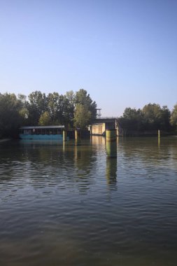 Kıyıların yanında demirleme direkleri ve güneşli bir günde İtalyan kırsalında ağaçlarla çevrili bir yol köprüsü olan saptırıcı bir kanal.