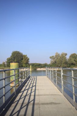 Oyalama kanalı üzerinde metalik tahta kaldırımlı iskele demirleme direklerinin yanında ve karşı kıyıda ağaçlarla çevrili.