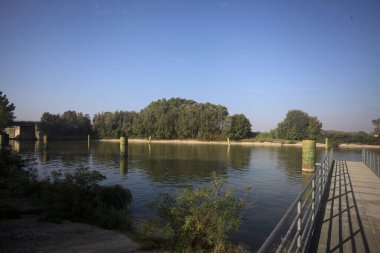 Oyalama kanalı üzerinde metalik tahta kaldırımlı iskele demirleme direklerinin yanında ve karşı kıyıda ağaçlarla çevrili.