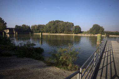 Oyalama kanalı üzerinde metalik tahta kaldırımlı iskele demirleme direklerinin yanında ve karşı kıyıda ağaçlarla çevrili.