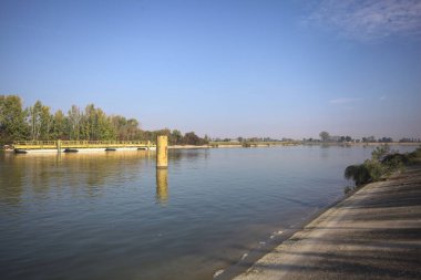 İtalya kırsalında güneşli bir günde beton kıyıdan görülen suya demirleme direkleri yansıyan saptırma kanalı.