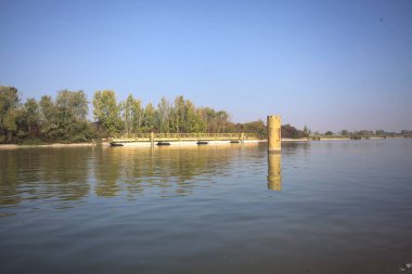 İtalya kırsalında güneşli bir günde beton kıyıdan görülen suya demirleme direkleri yansıyan saptırma kanalı.