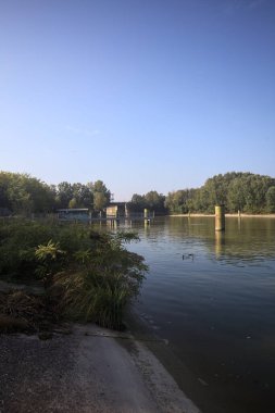 Kıyıların yanında demirleme direkleri ve güneşli bir günde İtalyan kırsalında ağaçlarla çevrili bir yol köprüsü olan saptırıcı bir kanal.
