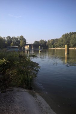 Kıyıların yanında demirleme direkleri ve güneşli bir günde İtalyan kırsalında ağaçlarla çevrili bir yol köprüsü olan saptırıcı bir kanal.