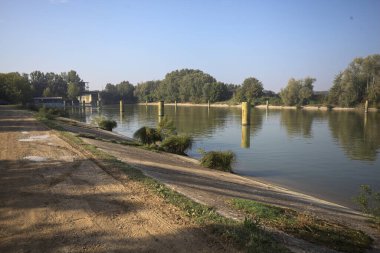 Kıyıların yanında demirleme direkleri ve güneşli bir günde İtalyan kırsalında ağaçlarla çevrili bir yol köprüsü olan saptırıcı bir kanal.