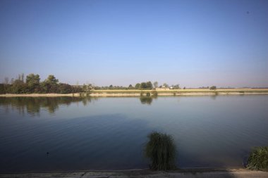 İtalya 'nın uzak bir kırsalında güneşli bir günde nehir kıyısında tarlalar ve kır malikaneleri üzerlerindeydi.
