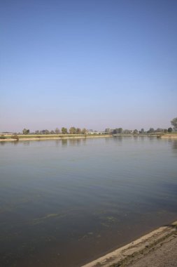 İtalya 'nın kırsal kesimlerinde güneşli bir günde ufuk çizgisi ve köprüsü olan küçük bir ada tarafından yapılan saptırıcı bir kanalda çatal.