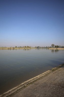 İtalya 'nın kırsal kesimlerinde güneşli bir günde ufuk çizgisi ve köprüsü olan küçük bir ada tarafından yapılan saptırıcı bir kanalda çatal.