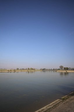 İtalya 'nın kırsal kesimlerinde güneşli bir günde ufuk çizgisi ve köprüsü olan küçük bir ada tarafından yapılan saptırıcı bir kanalda çatal.