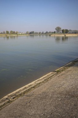 İtalya 'nın kırsal kesimlerinde güneşli bir günde ufuk çizgisi ve köprüsü olan küçük bir ada tarafından yapılan saptırıcı bir kanalda çatal.